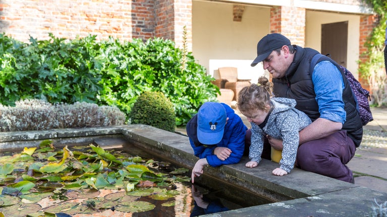 Man with two children bending over looking in a pond